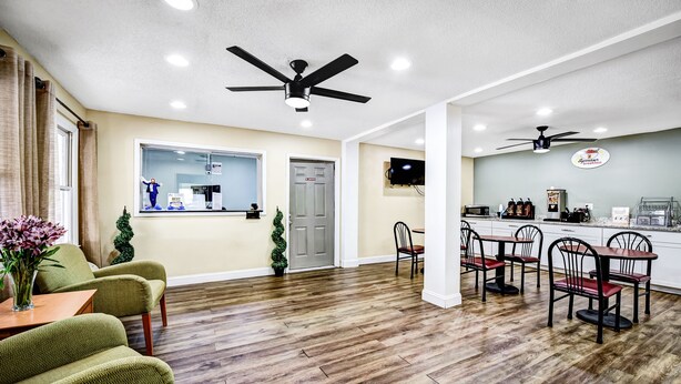 A spacious living area with a wooden floor, green armchairs, a dining table with chairs, a kitchen area with a bar, and ceiling fans. - Super 8 by Wyndham Manning (Manning)
