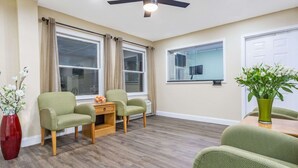 A room with two green armchairs, a wooden side table, a red vase with white flowers, and a wooden floor. - Super 8 by Wyndham Manning (Manning)