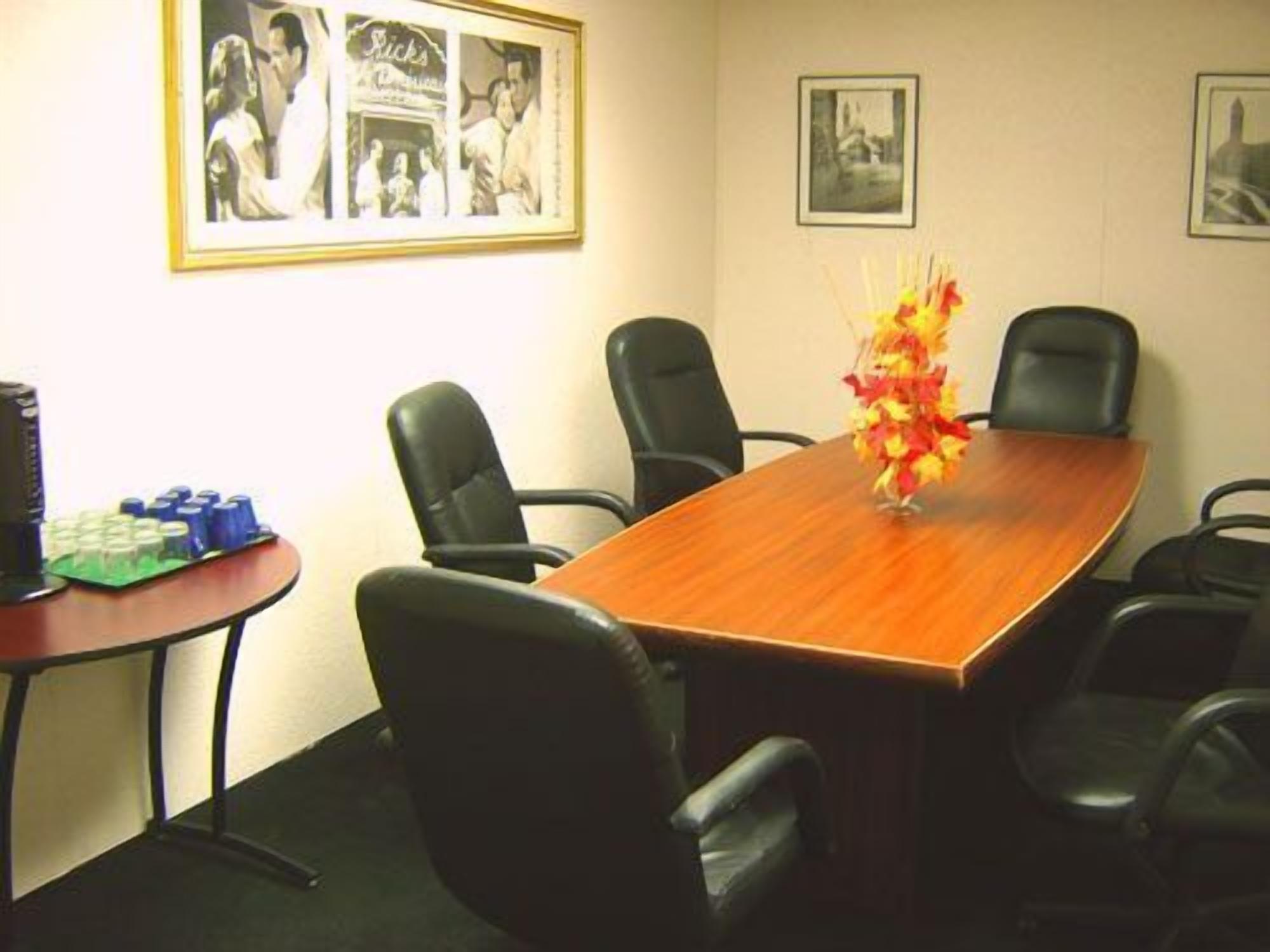 A conference room with a wooden table, black chairs, and a decorative vase. There are framed pictures on the wall and a small table with blue objects on the side.