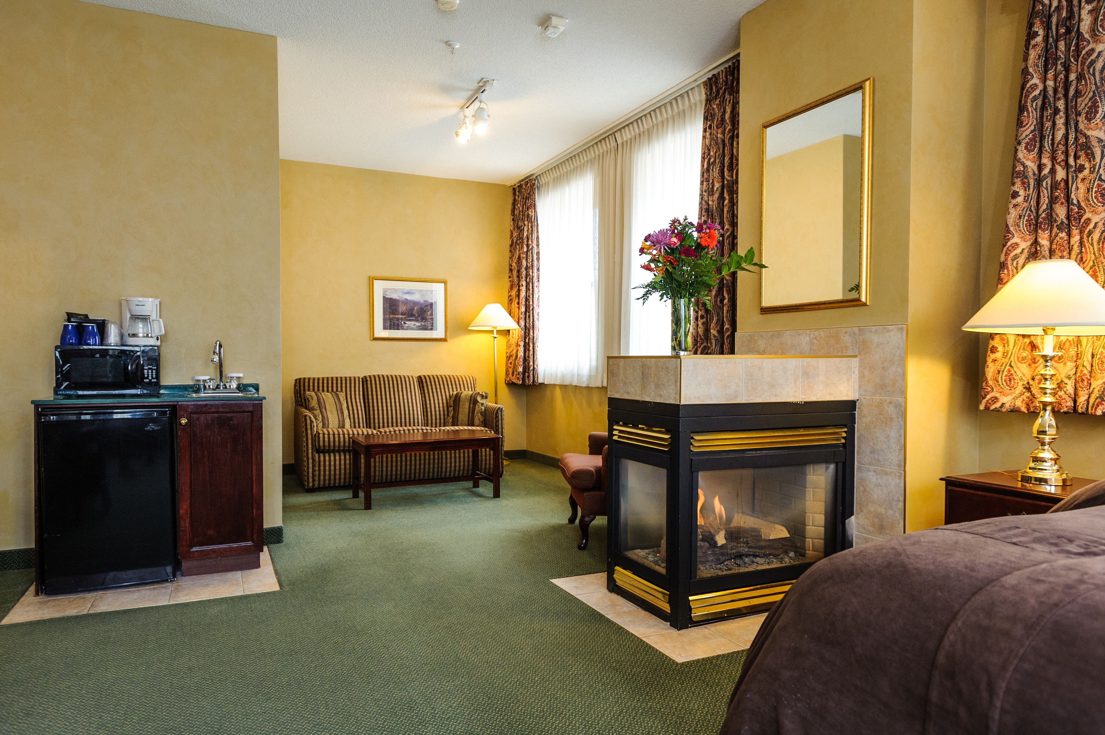A hotel room with a kitchenette, a sofa, a fireplace, and a bed.