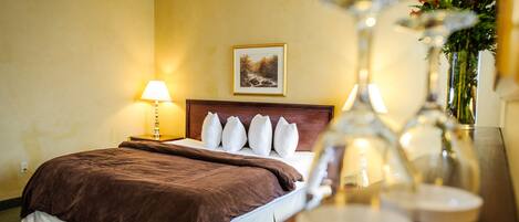 Una habitación de hotel con una cama, una mesita de noche con lámpara, un cuadro en la pared y un jarrón con flores sobre la mesa.