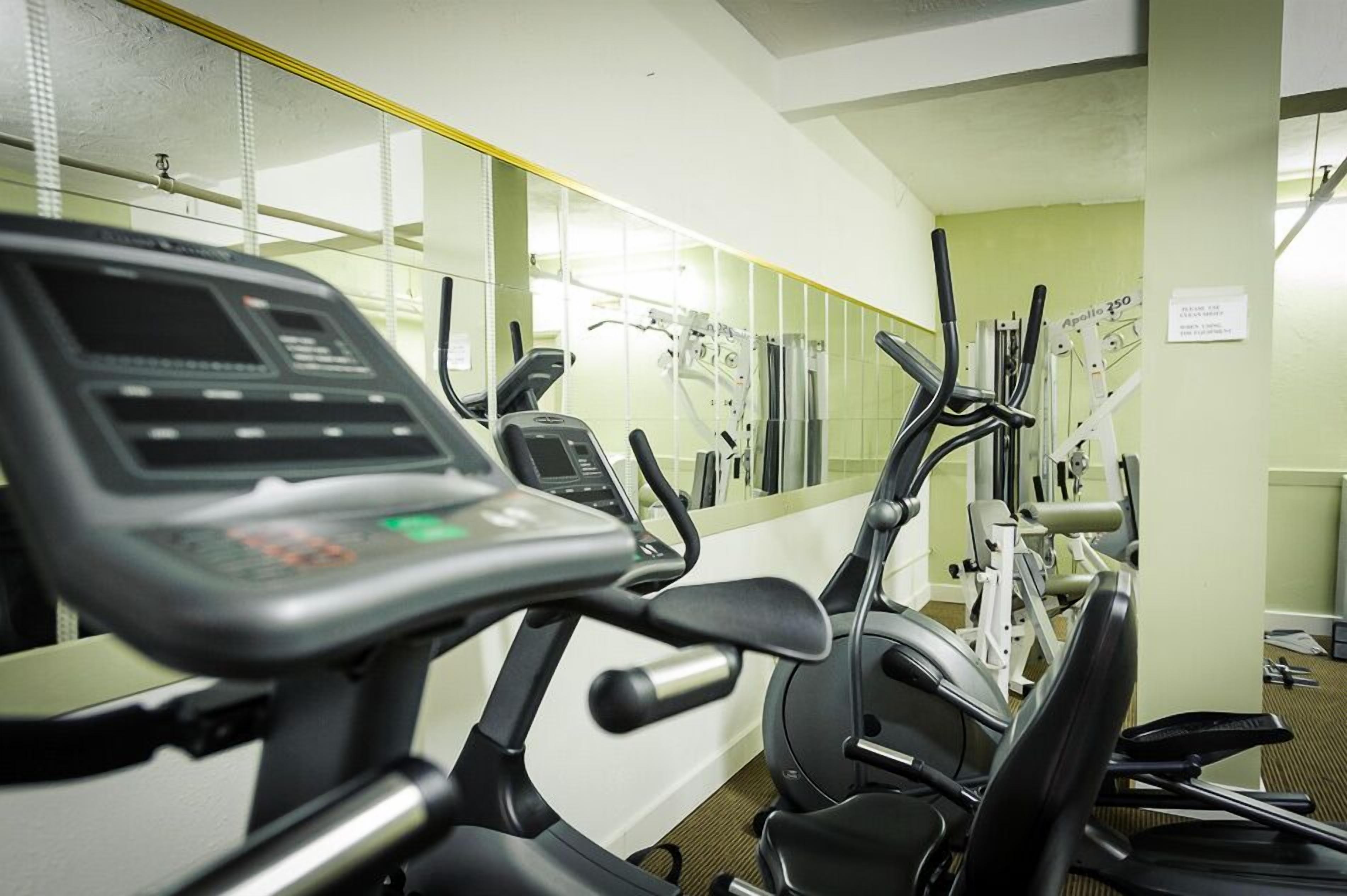 Ein Fitnessraum mit verschiedenen Trainingsgeräten, darunter Laufbänder und Crosstrainer, die in einer Reihe angeordnet sind.