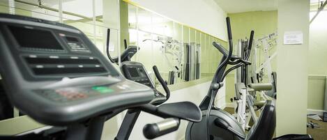 Ein Fitnessraum mit verschiedenen Trainingsgeräten, darunter Laufbänder und Crosstrainer, die in einer Reihe angeordnet sind.