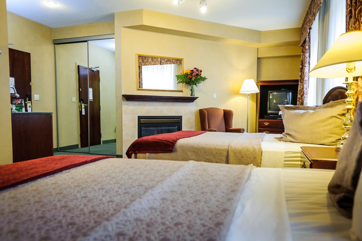 A hotel room with two beds, a fireplace, a TV, and a mirror.
