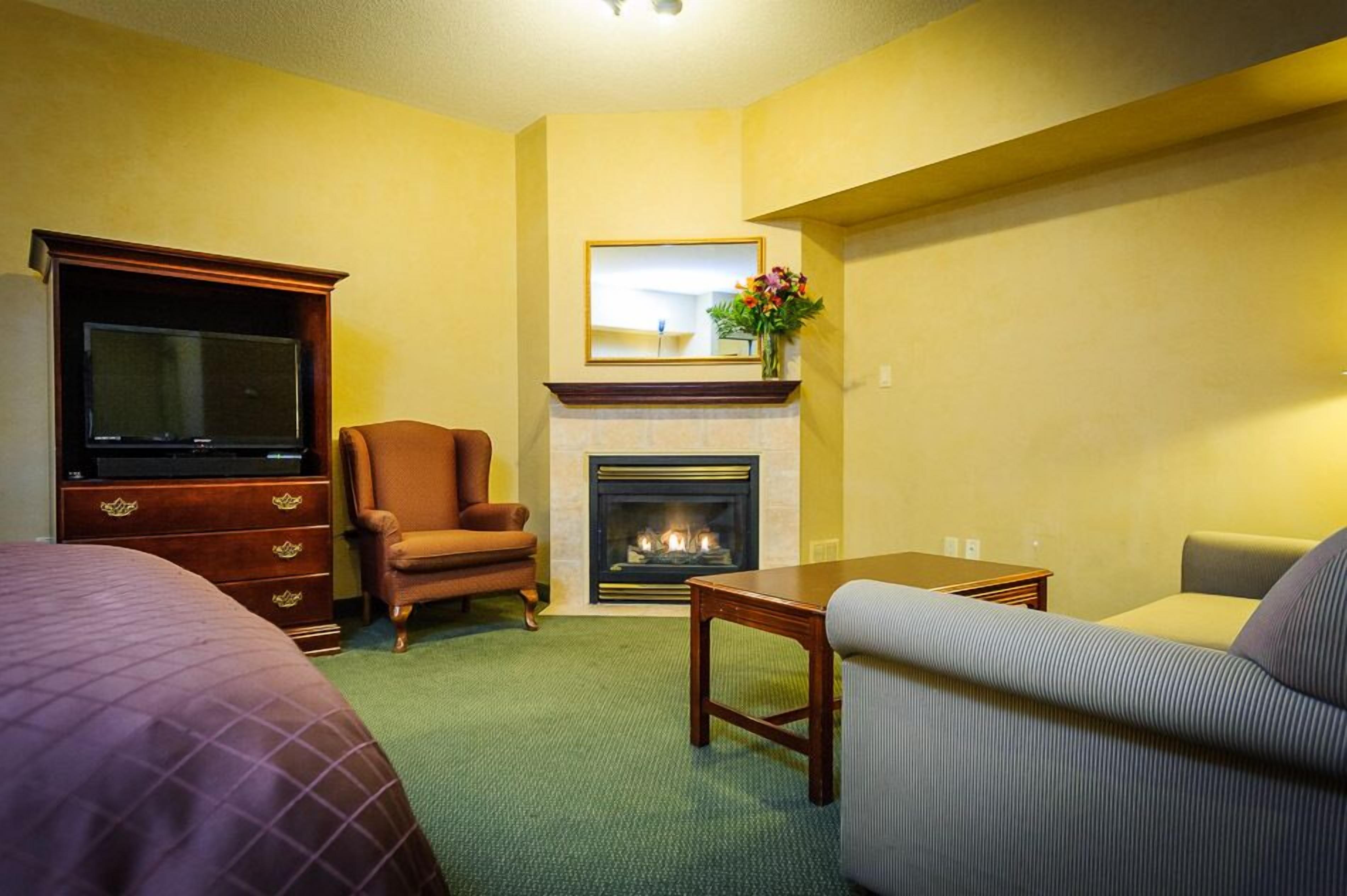 Una habitación de hotel con chimenea, televisión, sofá y cama.