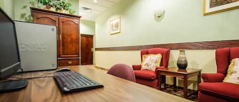 Habitación de hotel con un escritorio de madera, una computadora Dell, un sillón rojo y una mesita con un florero.