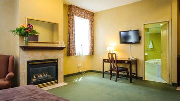 A hotel room with a fireplace, a television, a desk with a chair, and a bathroom visible through an open door.