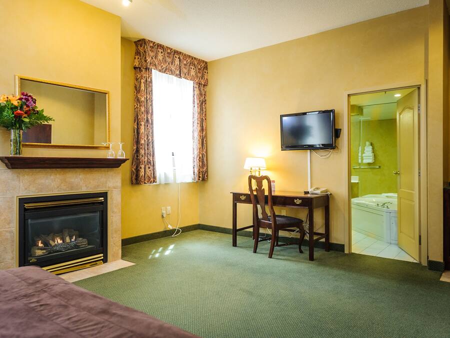 A hotel room with a fireplace, a television, a desk with a chair, and a bathroom visible through an open door.