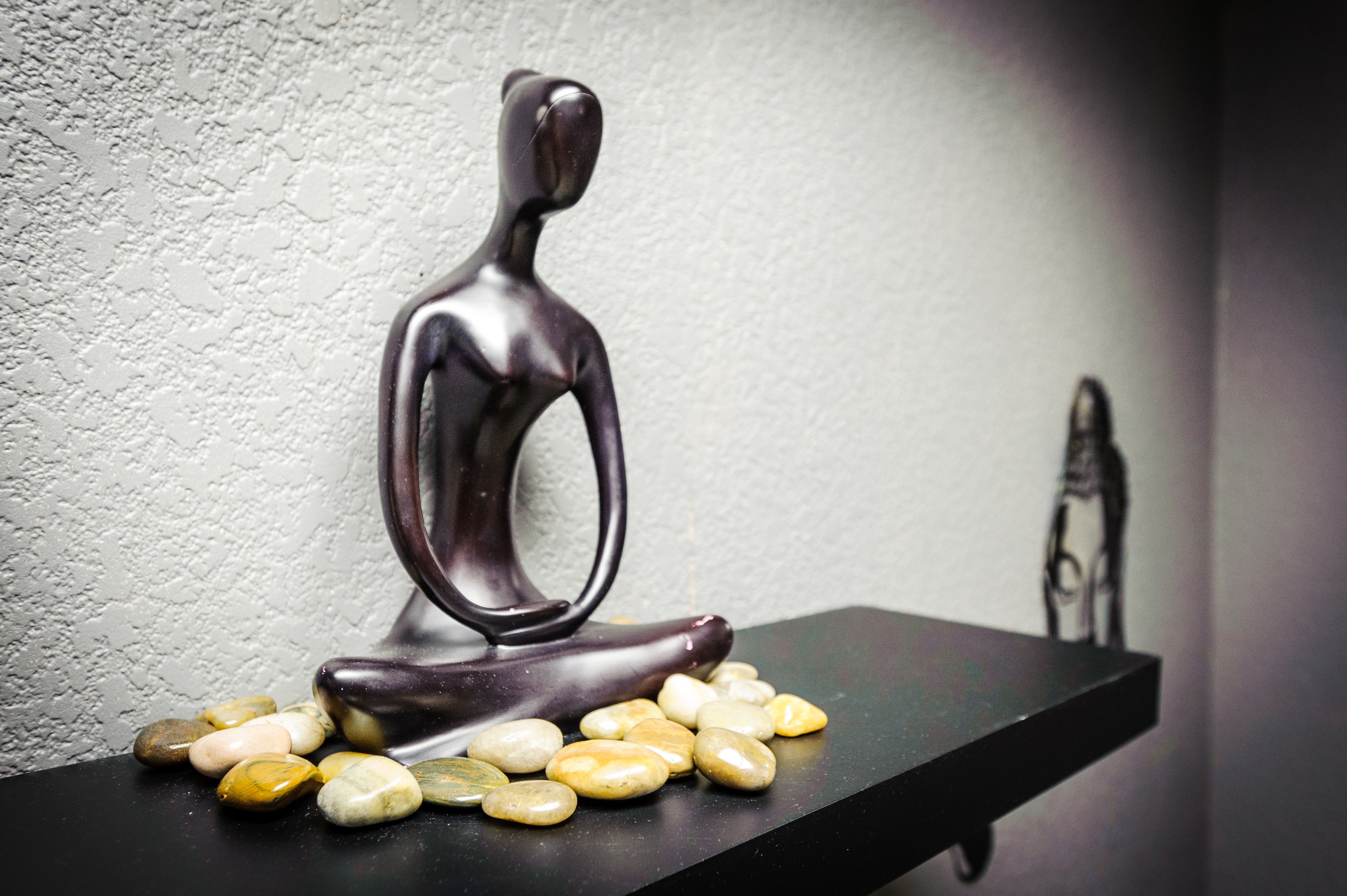 Uma escultura escura de uma figura sentada sobre uma prateleira preta, rodeada por pedras multicoloridas e lisas.