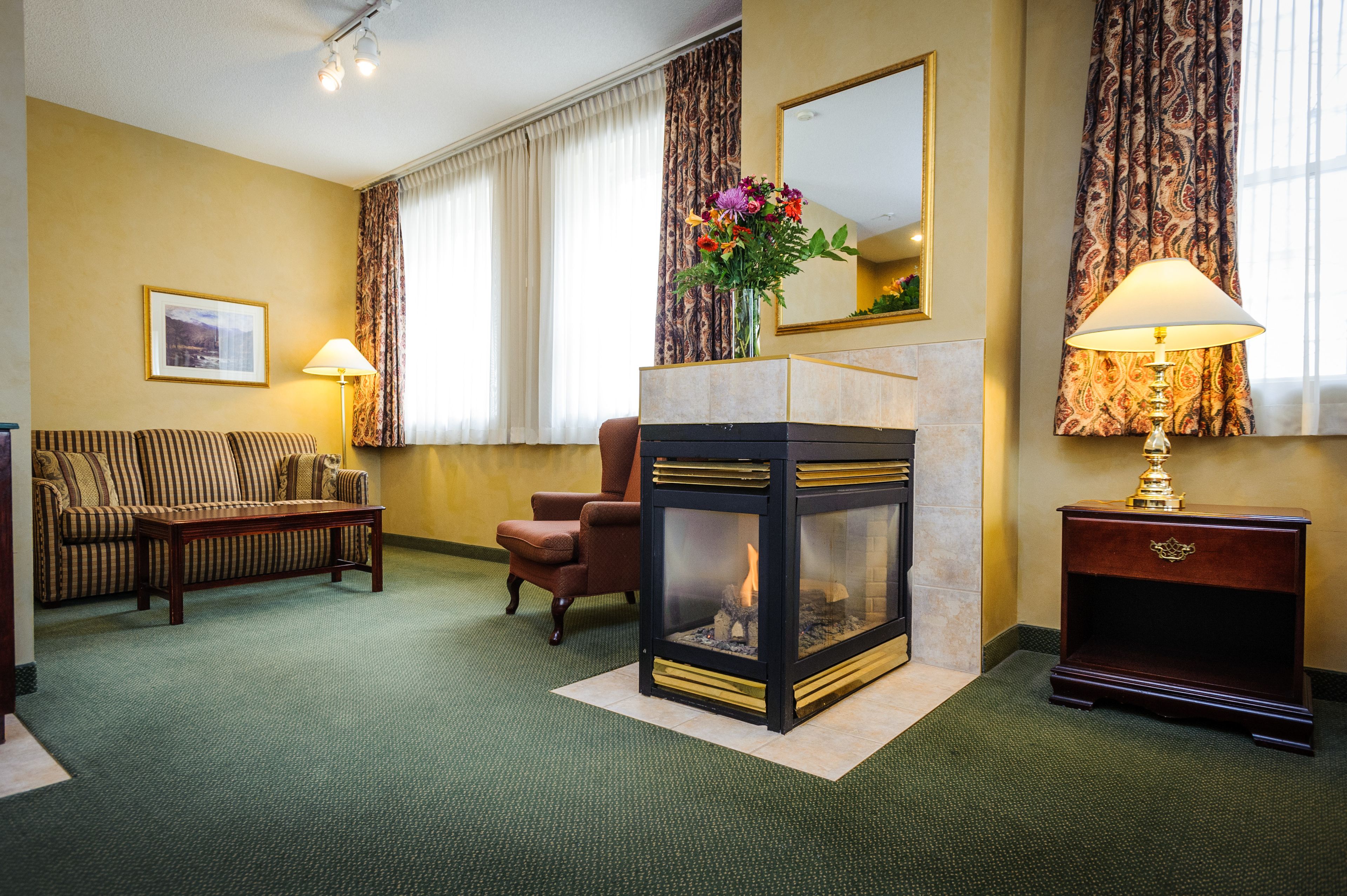 A hotel room with a sofa, armchair, fireplace, and a lamp.
