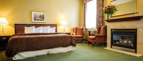 Un cuarto de hotel con una cama grande, dos sillones, una chimenea y un cuadro en la pared.