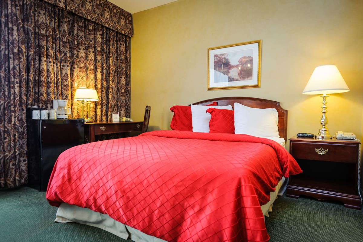 A hotel room with a large bed, two bedside tables, a desk with a lamp, and a picture on the wall.