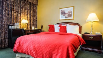 Habitación de hotel con una cama grande, dos mesitas de noche, un escritorio con lámpara y un cuadro en la pared.