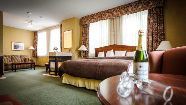 A hotel room with a large bed, a wooden desk, a sofa, and a table with a bottle of champagne. - Peterborough Inn & Suites Hotel (Peterborough)