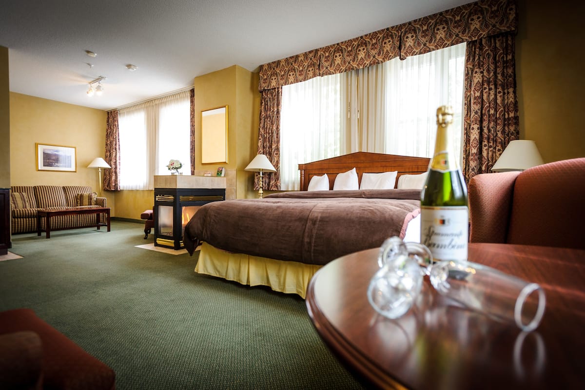 A hotel room with a large bed, a wooden desk, a sofa, and a table with a bottle of champagne.