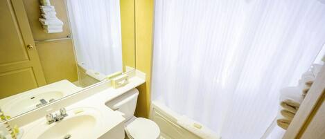 Une salle de bain avec un lavabo, des toilettes et une baignoire blancs, agrémentée d’un mur d’accent jaune et d’un rideau de douche blanc.