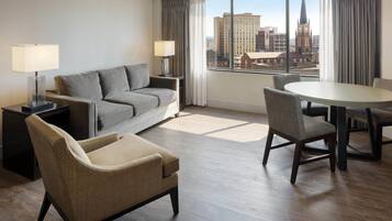A hotel room with a sofa, armchair, dining table, and chairs.