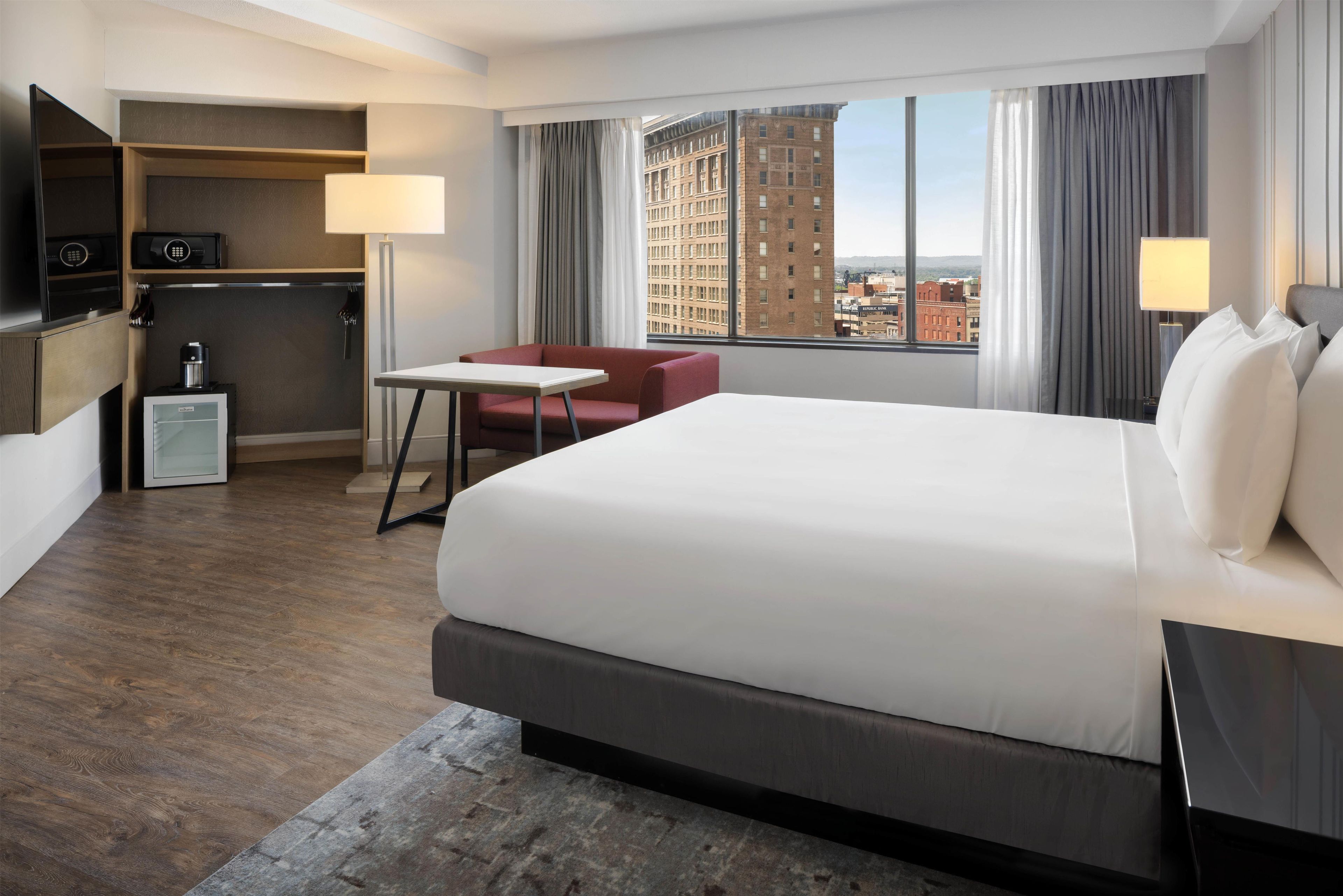 Habitación de hotel con una cama grande, un escritorio, una silla, un minibar y vistas a la ciudad.