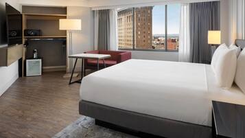 Habitación de hotel con una cama grande, un escritorio, una silla, un minibar y vistas a la ciudad.