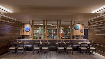 Uma área de bar com painéis de madeira, diversos arranjos de assentos e uma variedade de garrafas de bebidas alcoólicas expostas em prateleiras.