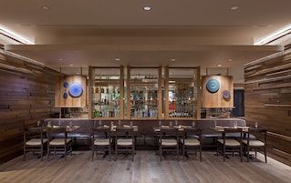 A bar area with wooden paneling, multiple seating arrangements, and a variety of liquor bottles displayed on shelves.