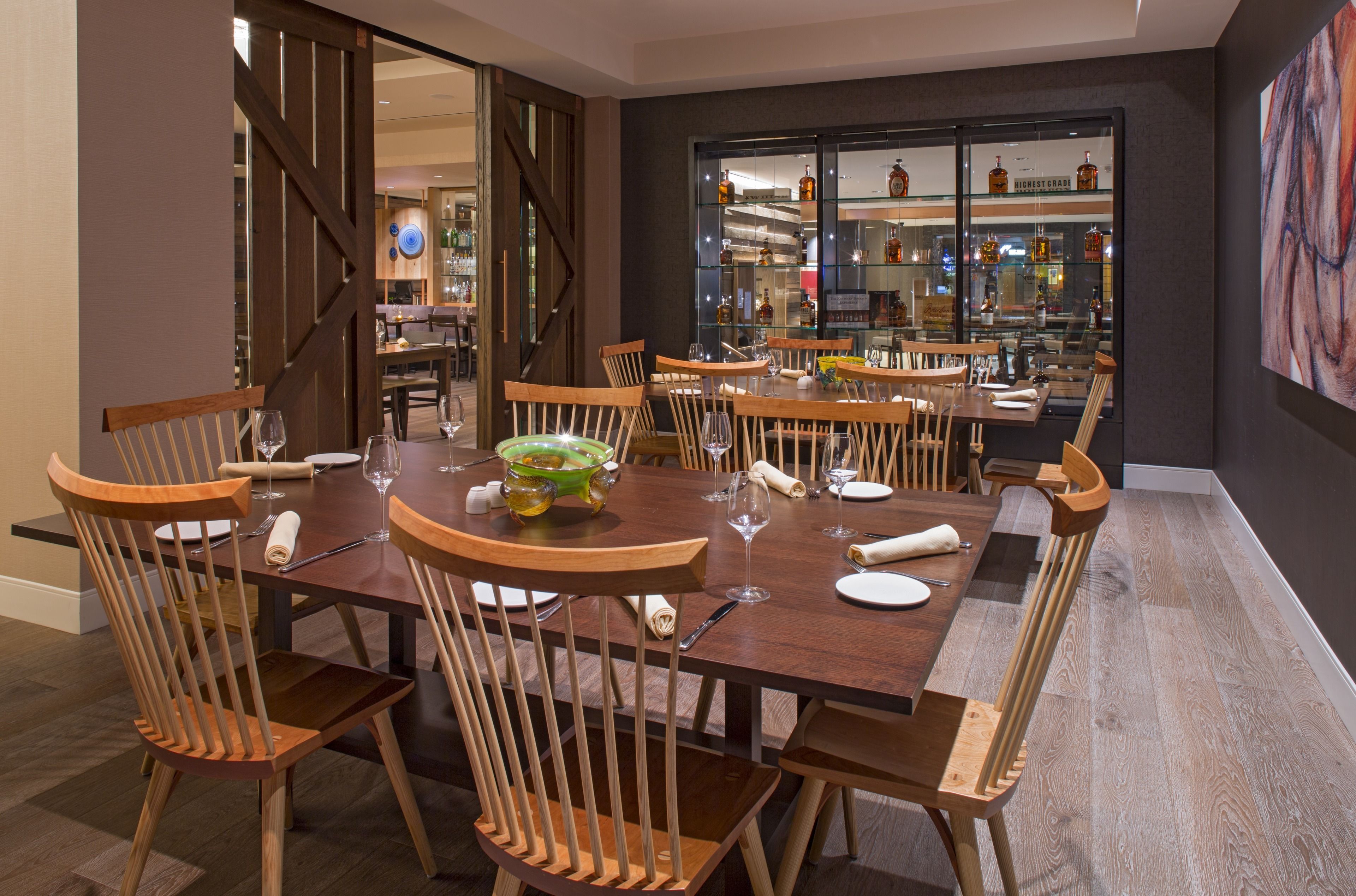 A dining area with a wooden table and chairs, a glass display case with bottles, and a view of the bar area.