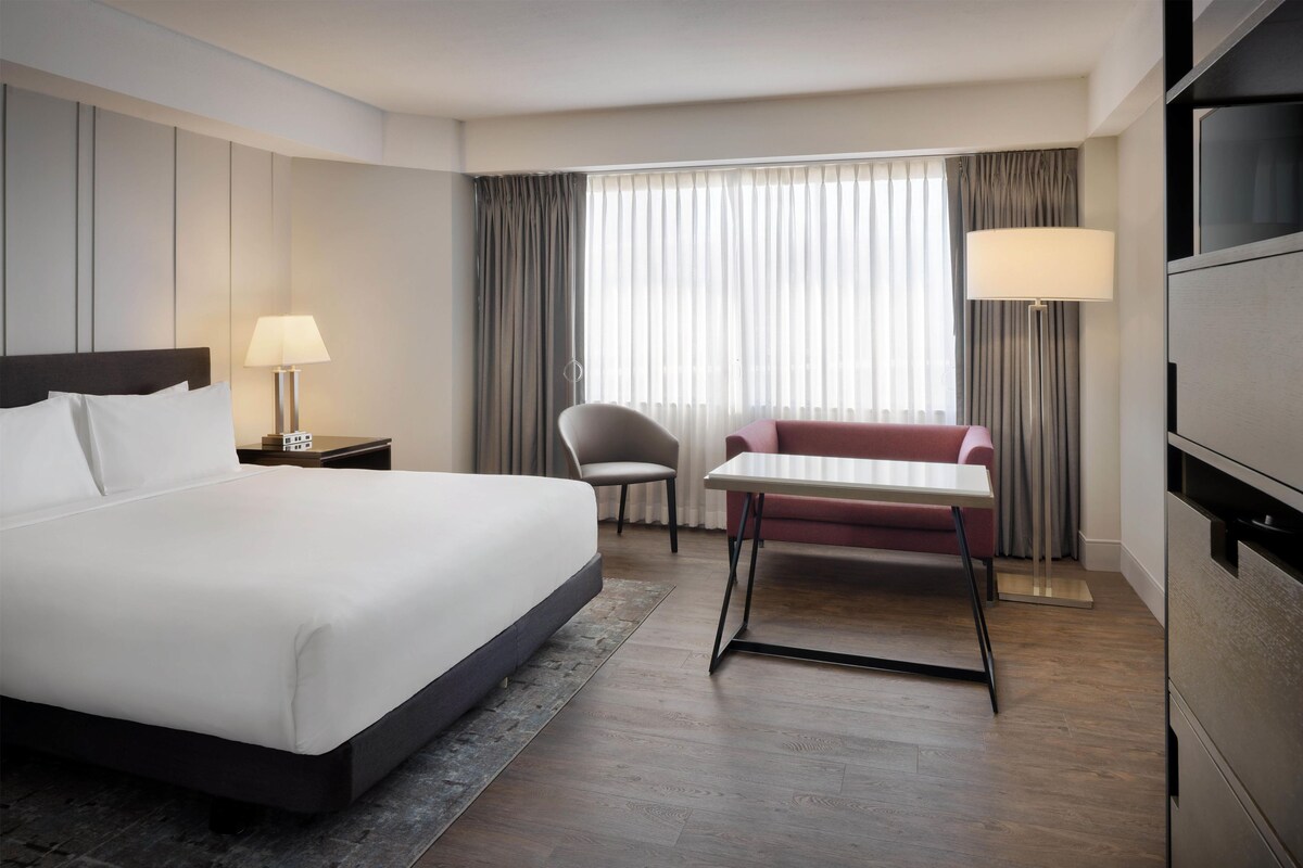 A hotel room with a large bed, a desk, a chair, a sofa, and a TV.