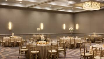 A banquet hall with round tables, gold chairs, and floral centerpieces.