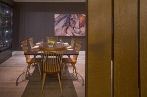 Een eetruimte met een ronde tafel, zes houten stoelen en een groot abstract schilderij aan de muur.