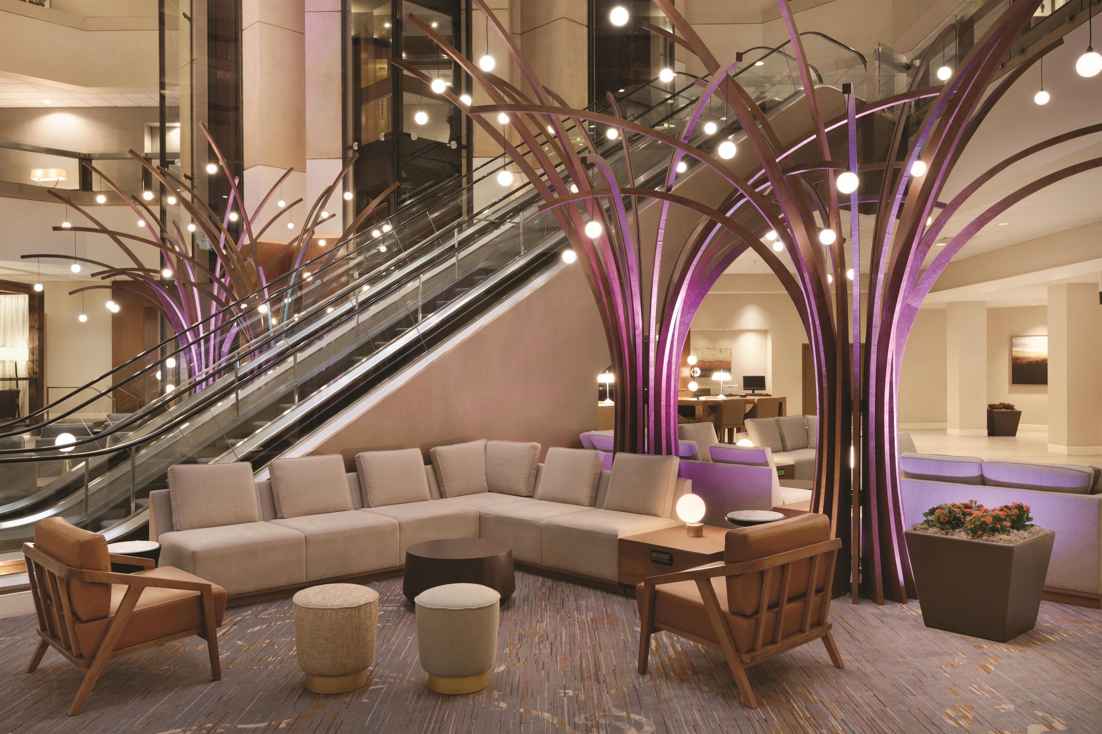 A modern lobby with a central seating area, an escalator, and a staircase.