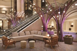 A modern lobby with a central seating area, an escalator, and a staircase. - Hyatt Regency Louisville (Louisville)