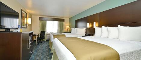 A hotel room with a large bed, a desk with a computer, a television, and a window with curtains.