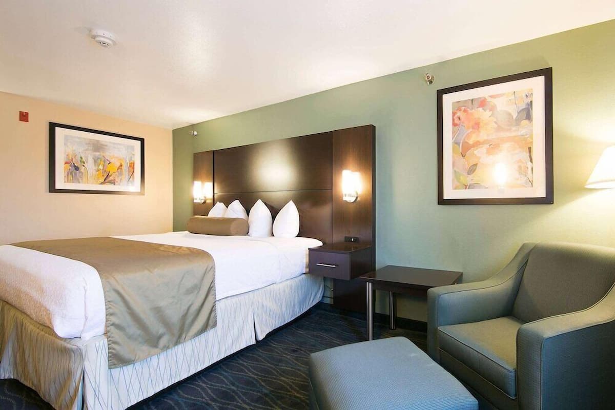 Quarto de hotel com uma cama grande, uma escrivaninha, uma cadeira e duas luminárias fixadas na parede.