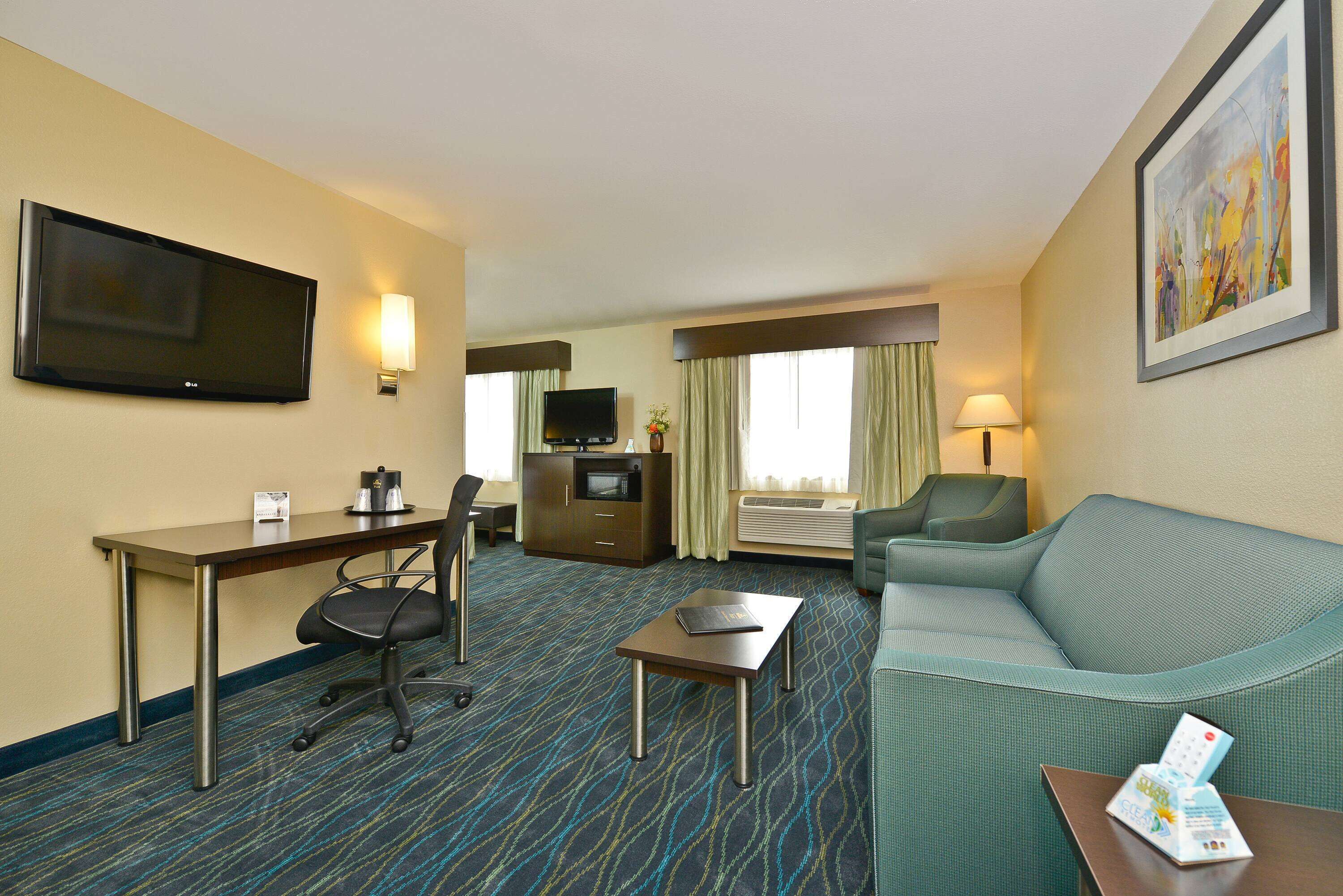 A hotel room with a flat-screen TV, a desk with a chair, a sofa, a small table, and a framed picture on the wall.