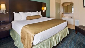 Une chambre d’hôtel avec un grand lit, une table de chevet, une commode et une salle de bain visible à travers une arche.