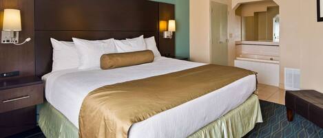 A hotel room with a large bed, a nightstand, a dresser, and a bathroom visible through an archway.