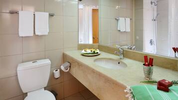 Un baño con inodoro, lavabo y ducha. Hay toallas colgadas en la pared y una toalla verde en la encimera.