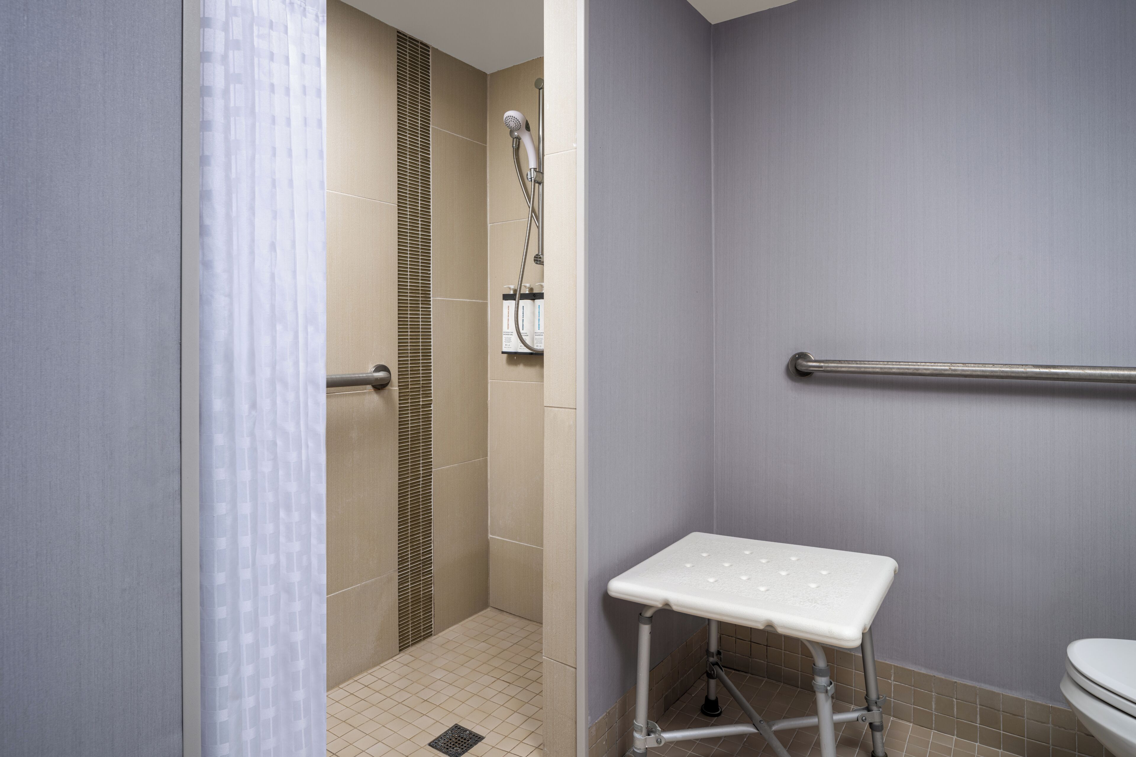 Un baño con ducha, inodoro y un banco blanco.