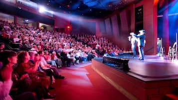 An auditorium with rows of seated attendees, a stage with performers, and a red carpet leading to the stage.