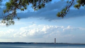 A calm lake with a sandy beach, a distant tower, and a cloudy sky.