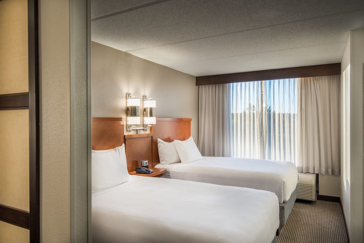 Ein Hotelzimmer mit zwei Betten, einem Nachttisch, einer Lampe und einem Fenster mit Vorhängen.