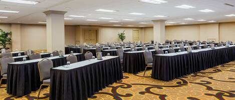 A conference room with rows of tables, chairs, and a carpeted floor.