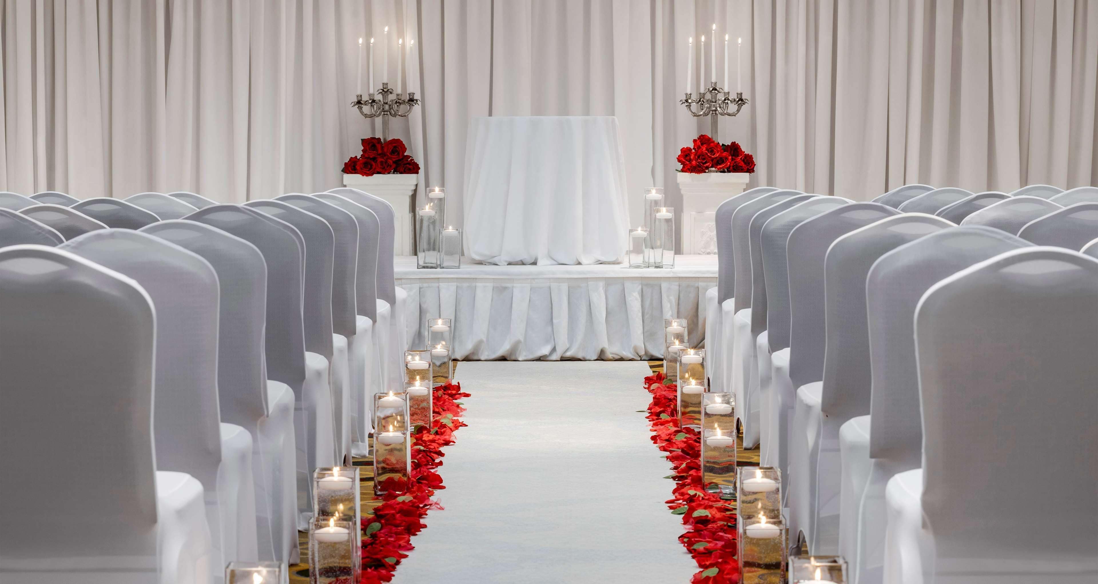 Un pasillo de bodas con sillas blancas, un altar blanco y flores rojas.
