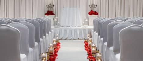 Un pasillo de bodas con sillas blancas, un altar blanco y flores rojas.