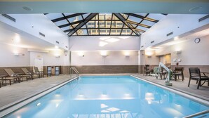 A swimming pool with a skylight, lounge chairs, and a clock on the wall. - Hilton Indianapolis Hotel & Suites (Indianapolis)