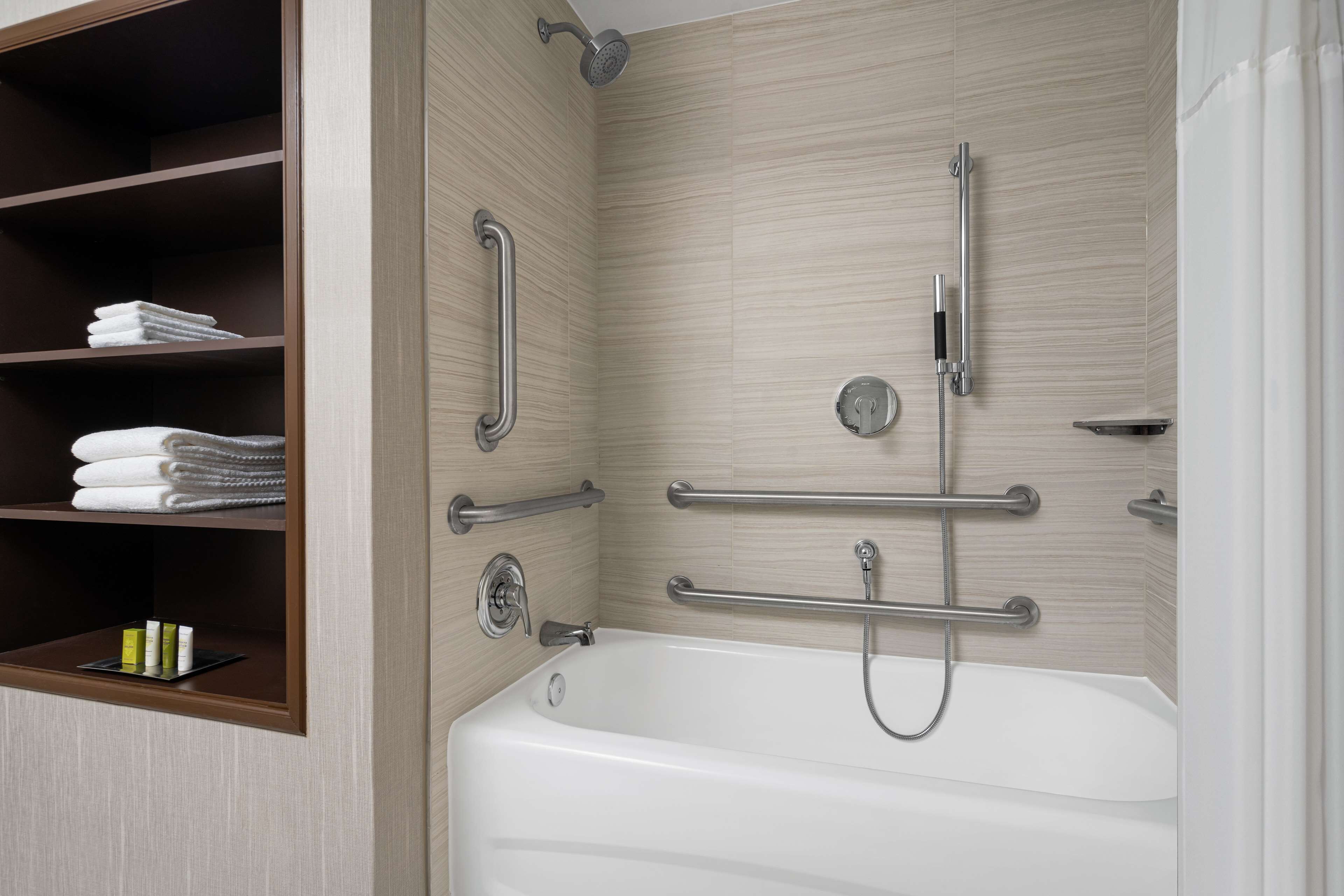 A modern bathroom with a bathtub, grab bars, and shelves with towels.