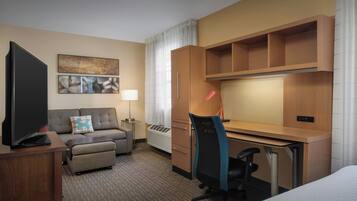 Habitación de hotel con cama, escritorio, silla, televisor, sofá, lámpara y un cuadro en la pared.