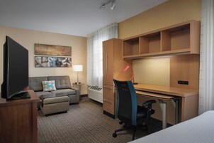 Habitación de hotel con cama, escritorio, silla, televisor, sofá, lámpara y un cuadro en la pared.