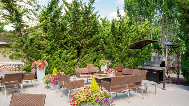 Un patio al aire libre con muebles de mimbre, una parrilla y plantas en macetas.