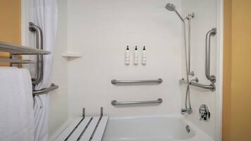 A bathroom with a white bathtub, grab bars, a showerhead, and three bottles of shampoo.